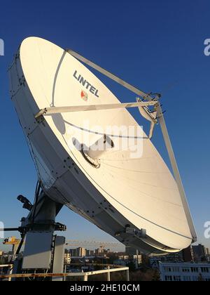 Huge retro satellite parabolic dish antenna on the roof for high speed internet link in front of blue sky Stock Photo