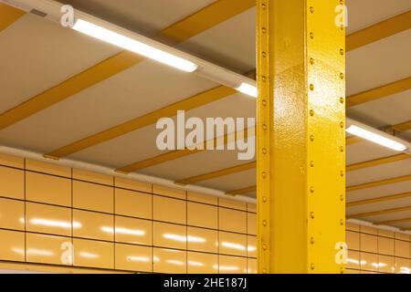 Closeup of a vertical yellow metal pole with a modern white ceiling in U Weberwiese station, Germany Stock Photo
