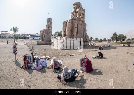 At the Colossi of Memnon historical site, a group of egyptian art students sit and draw the ancient statues in their sketch pads. Stock Photo