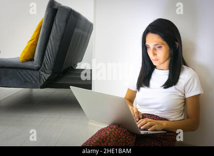 Young caucasian beautiful woman sits focused on the floor and types to notebook Stock Photo