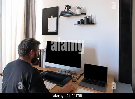 A Caucasian man sits at a desk at the home office looking at a computer screen. The great resignation concept. A male works on a computer online workplace. Mockup Copy Space. Hebrew English keyboard. Stock Photo
