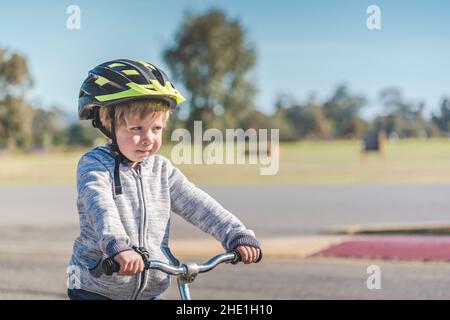 Portrait of a child wearing a helmet while riding his balance bike on the track in Adelaide Park Lands on a day, South Australia Stock Photo