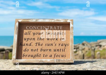 Motivational and inspirational quote on wooden frame with blurred background of ocean - Concentrate all your thoughts upon the work in hand. The sun r Stock Photo