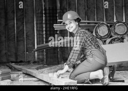 kid sawing a plank in carpentry. working with wood in a garage. happy childhood. hardworking child sawing with hand wood saw. teenage girl with hand Stock Photo