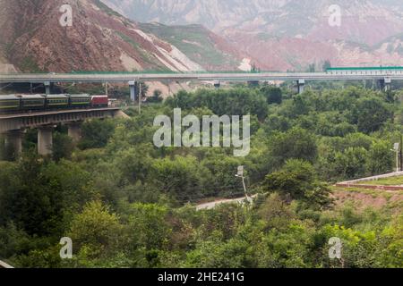 Train passing under a highway bridge in Hekou near Lanzhou, Gansu Province, China Stock Photo