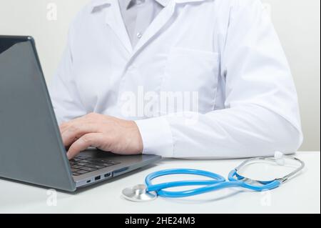 Male doctor at work in clinic office. Man professional medic physician wearing white coat and stethoscope working on computer at workplace. Doctor wor Stock Photo