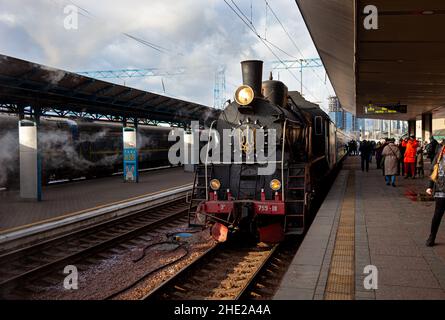 Ukraine, Kyiv - January 7, 2022: Retro train smokes on the platform of the central railway station. Old steam locomotive on the platform. Emblem of Ukraine. Smoke comes out of the chimney. Stock Photo