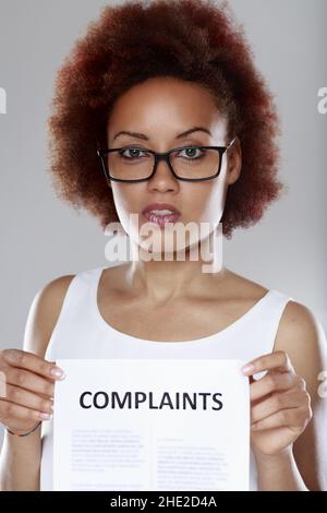 Unhappy young Black woman wearing glasses holding a list of Complaints to her chest in close up Stock Photo