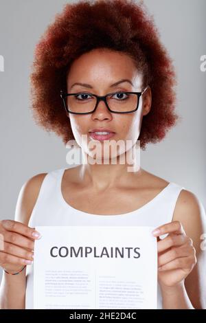 Dissatisfied young Black woman wearing spectacles holding a list of Complaints visible to the viewer Stock Photo