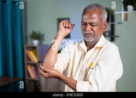 indian senior old man exercising by strenching hand due to elbow joint pain at home - concept of suffering joint pain and sprain injury. Stock Photo