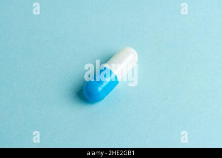 White-blue pill capsule on blue background. Minimal pharmacy concept. Flat lay. Stock Photo