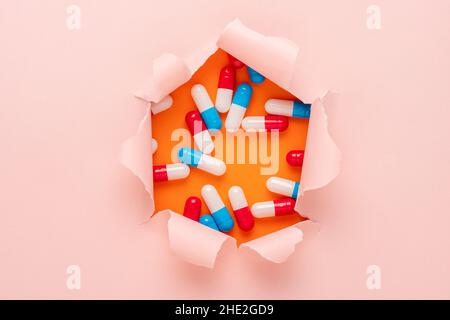 Vivid pink ripped paper with colorful pills on orange background. Minimal creative concept. Stock Photo