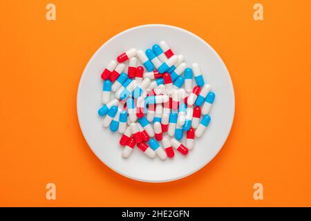 Colorful pills on white plate on orange background. Minimal concept. Stock Photo