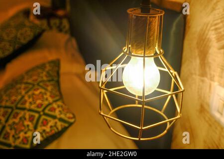 Golden Metal decorative lamp with a bright lamp over the bed with pillows. hotel bedroom. Switched on lamp close-up. Light equipment Stock Photo