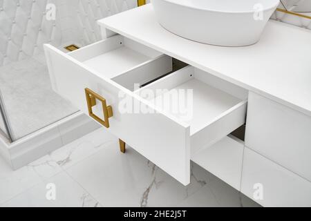 Elegant white cabinet with open drawer and shiny golden handles and leg with vessel sink in contemporary bathroom closeup Stock Photo