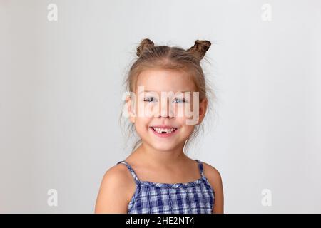 Portrait of happy caucasian child kid little girl of 5 years on grey background looking at camera showing her teeth without lost lower teeth. Concept Stock Photo