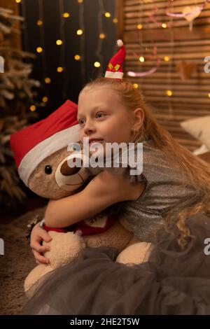 A girl hugs a bear toy in a Christmas cap bear Christmas kid child happy, for female young for play white fun, sleep plush. Gift woman happiness, rela Stock Photo