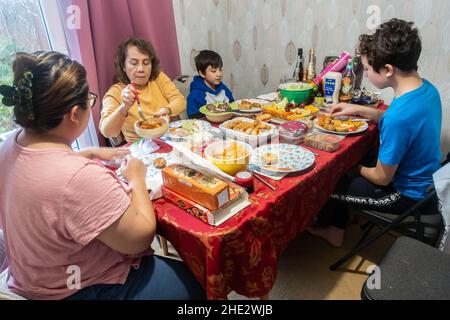 A family sit at a dining room table and eat together with a help yourself buffet style meal with a selection of different food items to choose from Stock Photo