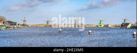 Panoramic view of a row of five Dutch windmills along the waterside at Zaanse Schans, Netherlands Stock Photo