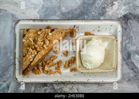 A slice of walnut cake and ice cream in a porcelain serving plate on a marble floor Stock Photo