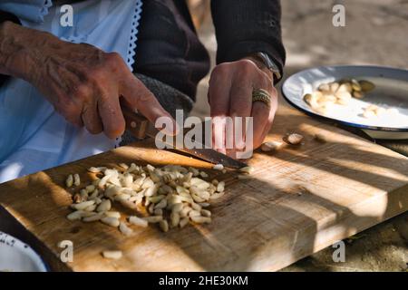Close up of the hands of an old woman that cuts almonds for sweets preparation Stock Photo