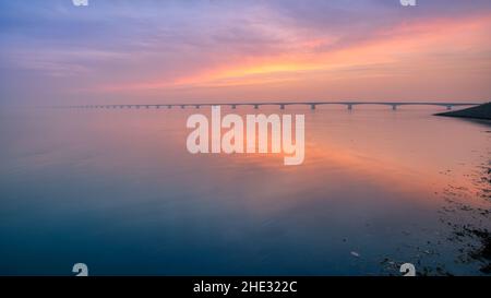 Long bridge over glassy smooth water  going to infinity over the magnificent ocean under the beautiful colorful sky in Zeeland, the Netherlands