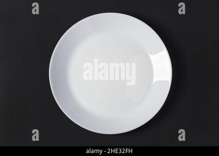 White porcelain plate on a black wooden table top. View from above Stock Photo