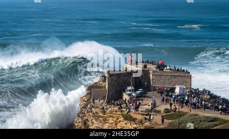 Giant waves breaking near the Fort of Sao Miguel Arcanjo Lighthouse in Nazare, Portugal. Nazare is famously known for having the biggest waves in the Stock Photo