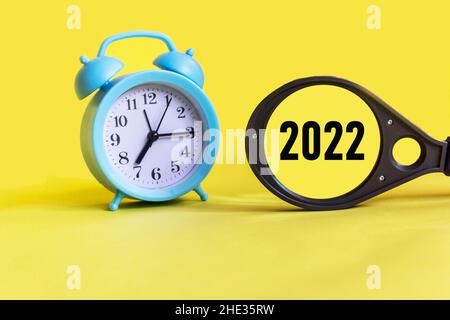 Magnifier with the number 2022 on a yellow background with an alarm clock. New year concept. Stock Photo