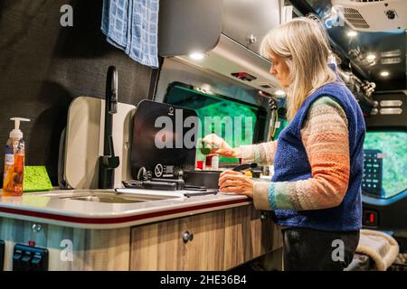 Woman cooking meal in Airstream Interstate 24X 4WD campervan; Ainsworth State Park; Columbia River Gorge; Oregon; USA Stock Photo