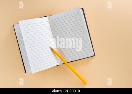 Open lined notebook with yellow pencil isolated on light brown background in top view, flat lay, copy space Stock Photo