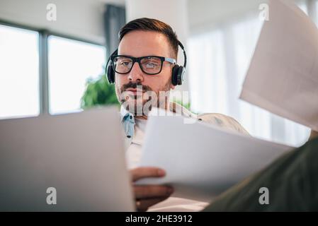 Thoughtful dedicated serious focused pensive man businessman entrepreneur working with printed documents and laptop computer making a online video cal Stock Photo