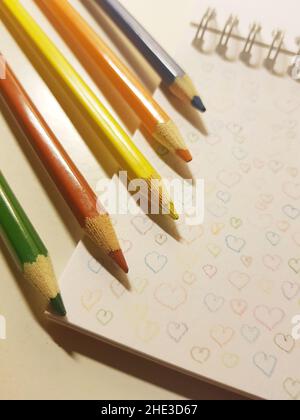 colored pencils on white notebook paper with drawn hearts. Stock Photo