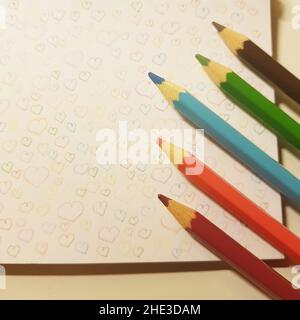 colored pencils on white notebook paper with drawn hearts. Stock Photo