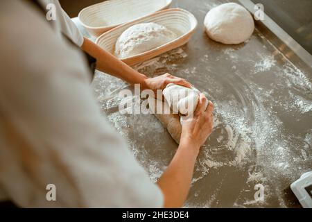 Professional baker kneads raw dough to make delicious bread in workshop Stock Photo