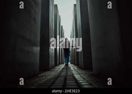 October 2021 - Berlin, Germany. Woman stands in dark maze between tall blocks in Holocaust Jewish Memorial of Murdered Jews. Light at the end of Stock Photo