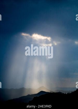 God beams or sun beams stream through a hole in dark clouds toward the ground in Tonto National Forest east of Phoenix Arizona. Stock Photo
