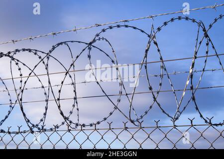 Barb wire rolls with razor blades mounted on a fence which surrounds a restricted and sensitive area Stock Photo