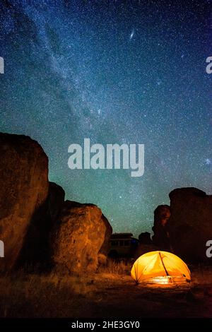 Milky way and other stars in night sky above rock formations and glowing tent at City of Rocks Sate Park, New Mexico. Stock Photo