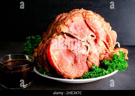 Glazed Spiral Cut Ham on Served with Sauce: A cooked spiral ham on a platter garnished with kale and served with glaze on the side Stock Photo