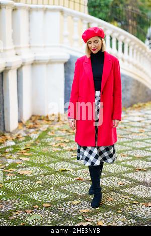 Middle-aged woman wearing red winter clothes walking through an urban park. Stock Photo