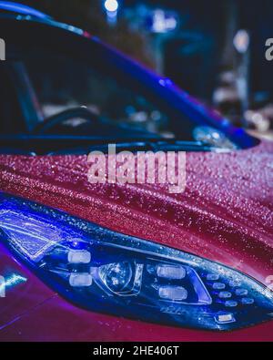 Rain drops on red car. Neon street lights reflecting on the car's surface. Stunning night photography. High quality photo Stock Photo