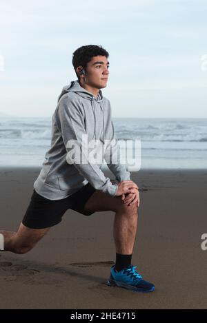 Hispanic young man stretching psoas and warming up at the beach. Stock Photo