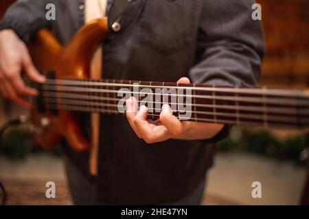 A young guy with a beard plays a bass guitar with five strings Stock Photo