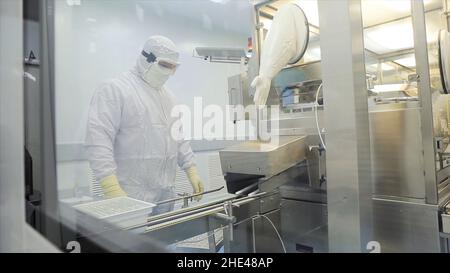 Worker in apron, cap, gloves with tablet checking process at production line in factory. Quality Control Workers Examining Pills in Lab. Pharmaceutica Stock Photo
