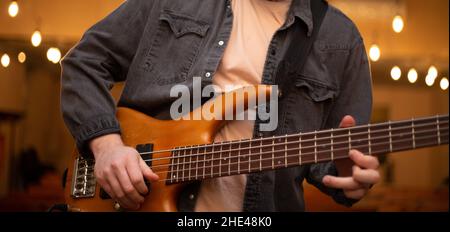 A young guy with a beard plays a bass guitar with five strings Stock Photo