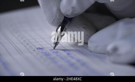 Side view of a hand making notes in a logbook. Close up of hands in white gloves writing data in the notebook with a pen on black background. Stock Photo