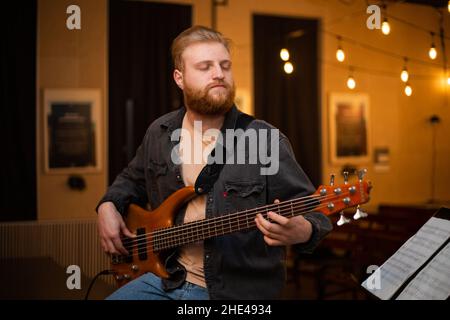A young guy with a beard plays a bass guitar with five strings Stock Photo