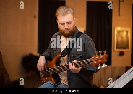 A young guy with a beard plays a bass guitar with five strings Stock Photo
