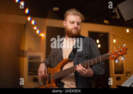 A young guy with a beard plays a bass guitar with five strings Stock Photo
